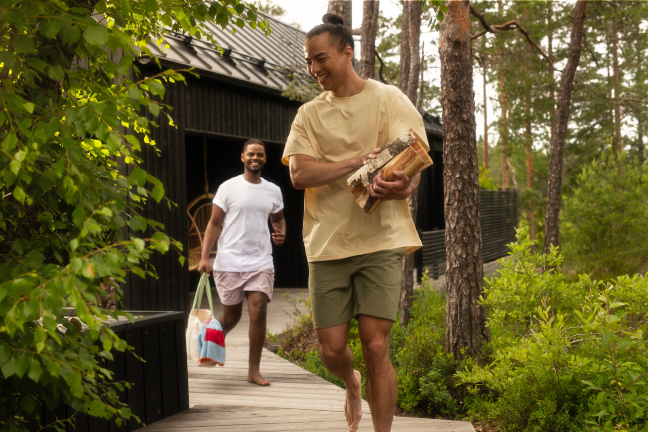 Kuvassa kaksi henkilöä kävelevät perätysten ja kantavat saunan halkoja.